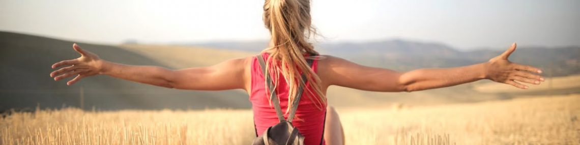 Woman enjoying the open air and freedom while sitting in a hay field during sunset.